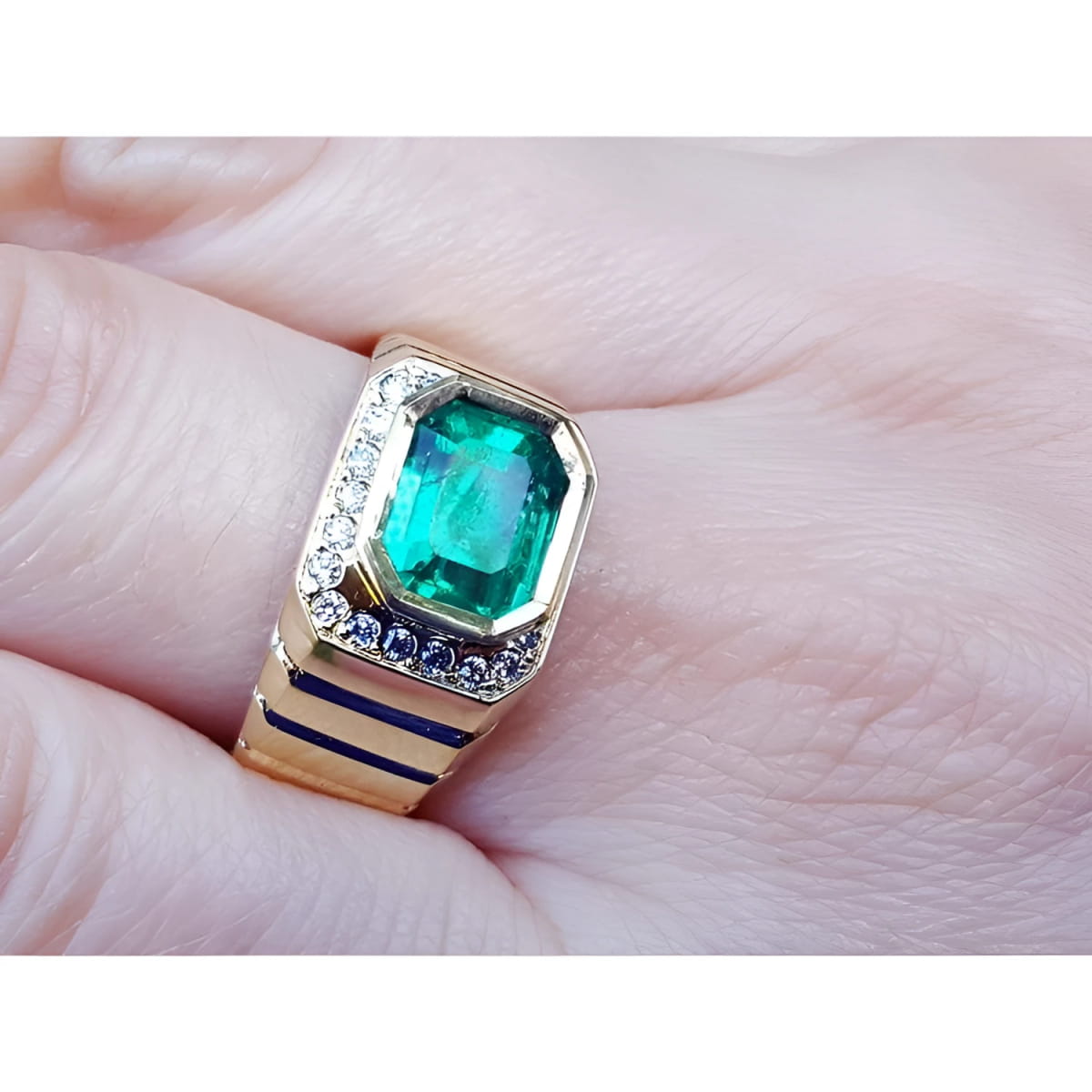An 18k yellow gold men’s emerald ring with sparkling accent diamonds resting on a finger.