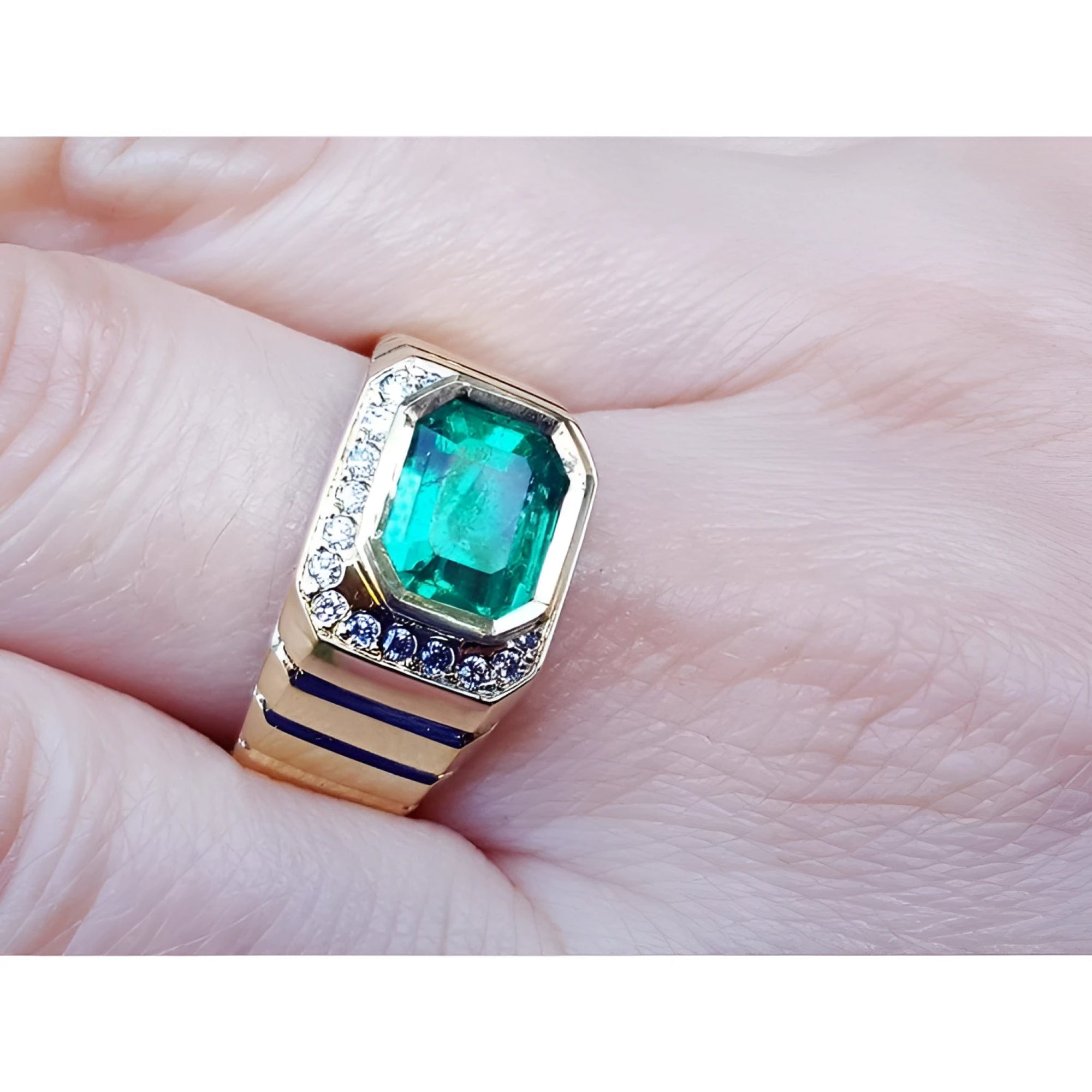 An 18k yellow gold men’s emerald ring with sparkling accent diamonds resting on a finger.
