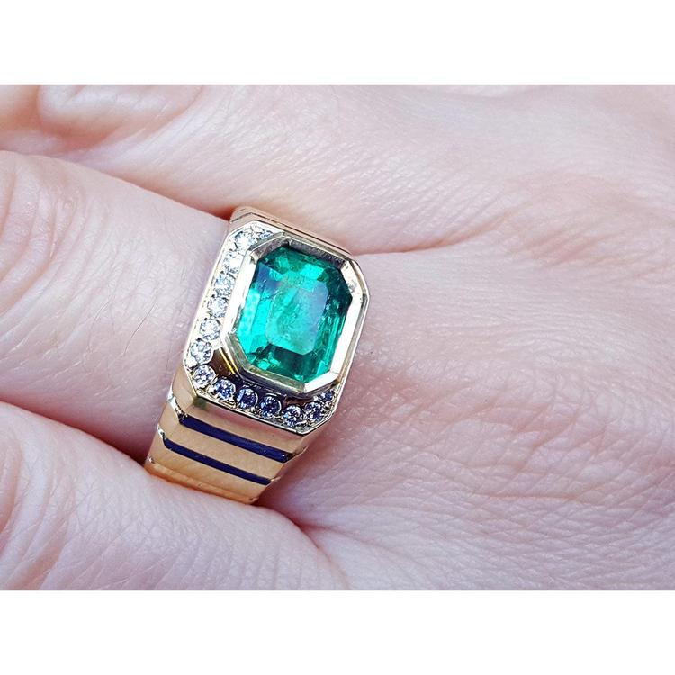 An 18k yellow gold men’s emerald ring with sparkling accent diamonds resting on a finger.