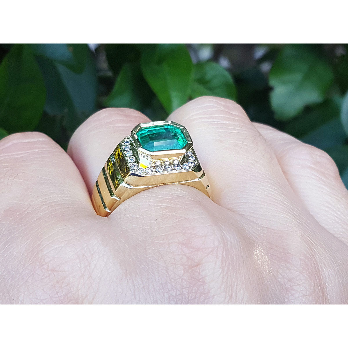 Gold ring 18k for men with a colombian emerald on a hand against a blurred green background.
