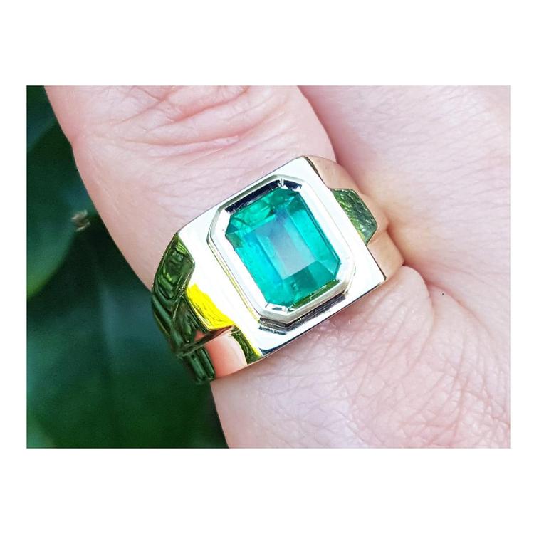 Gold ring with a rectangular emerald-cut on a finger against a blurred green background.