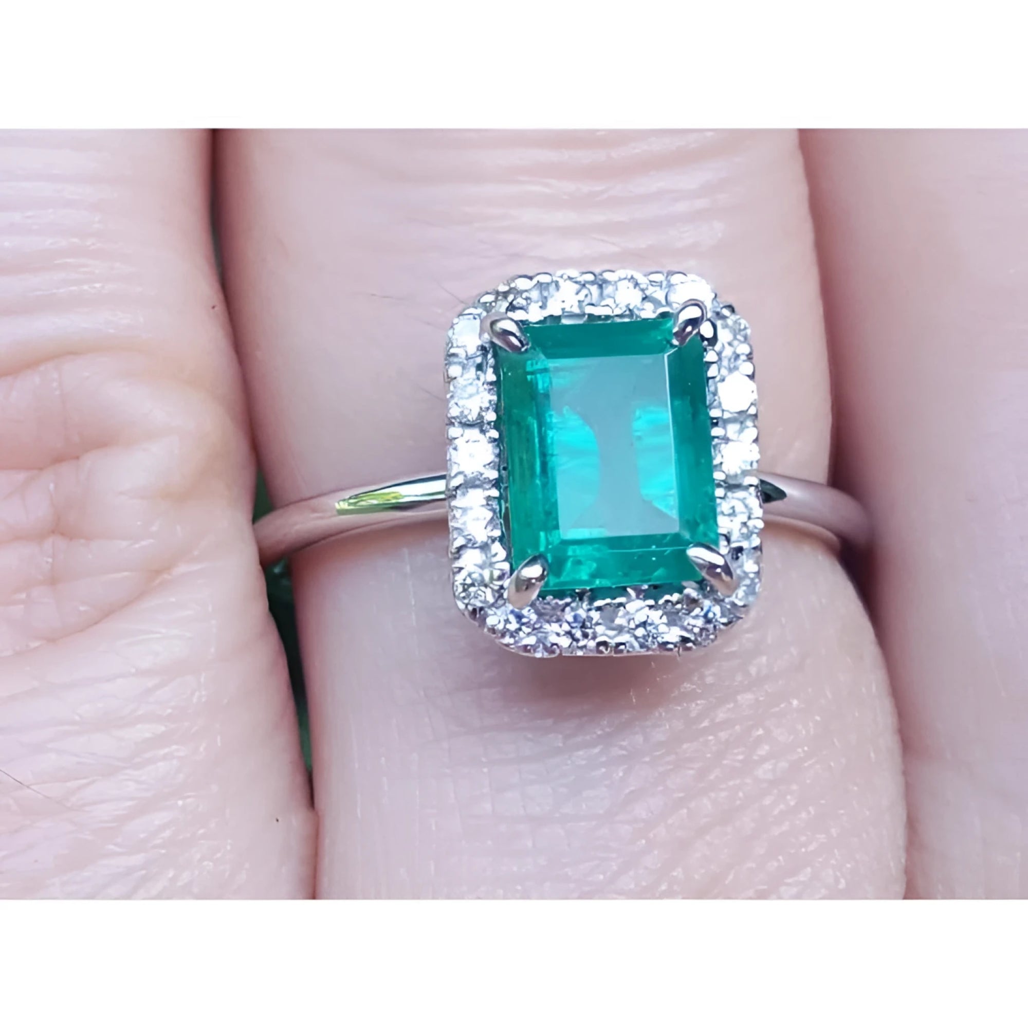 A natural Muzo colombian emerald ring with halo diamond in white gold on a finger.