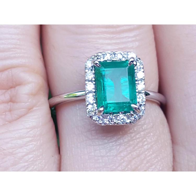 A natural Muzo colombian emerald ring with halo diamond in white gold on a finger.