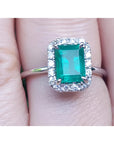 A natural Muzo colombian emerald ring with halo diamond in white gold on a finger.