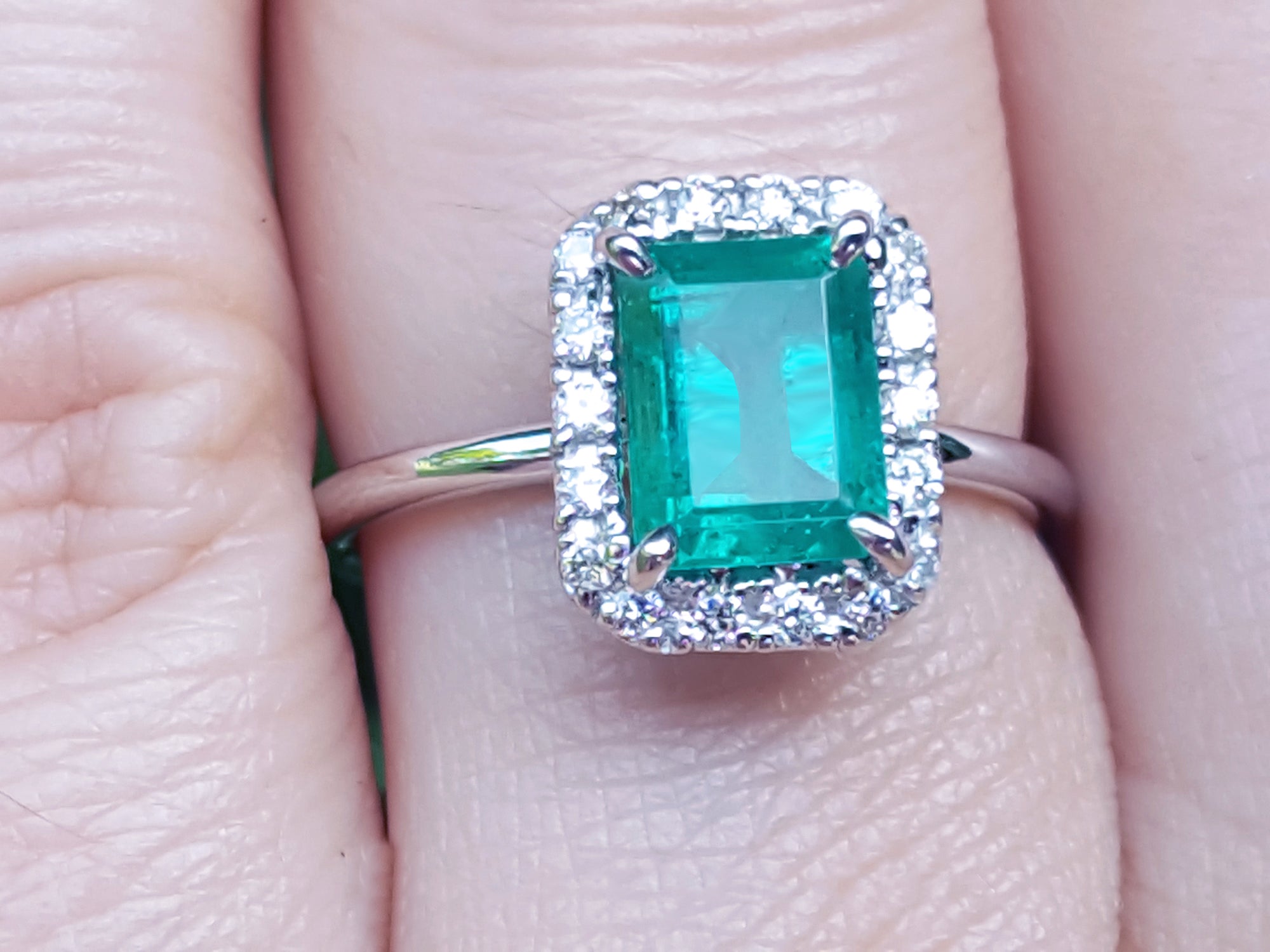 Emerald ring with halo diamond on a finger.