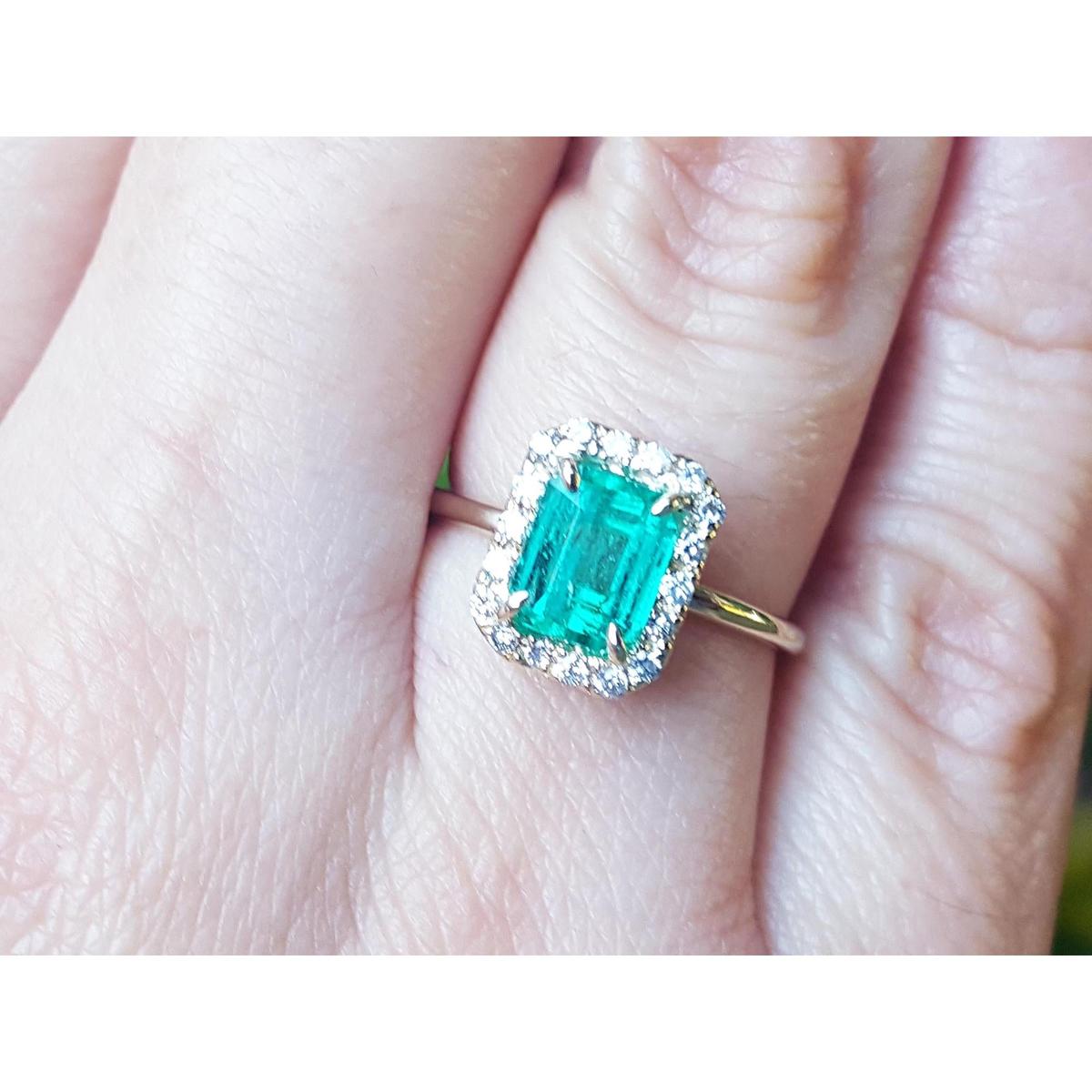 A close-up of a halo diamond emerald ring on a person's finger.