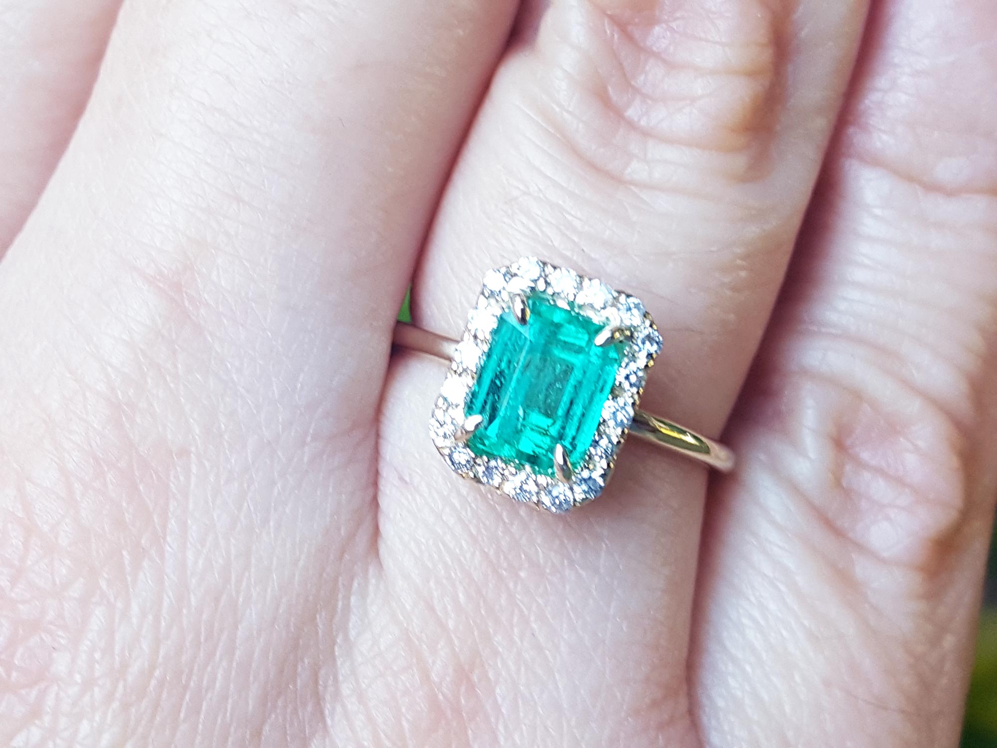 A close-up of a halo diamond emerald ring on a person&#39;s finger.
