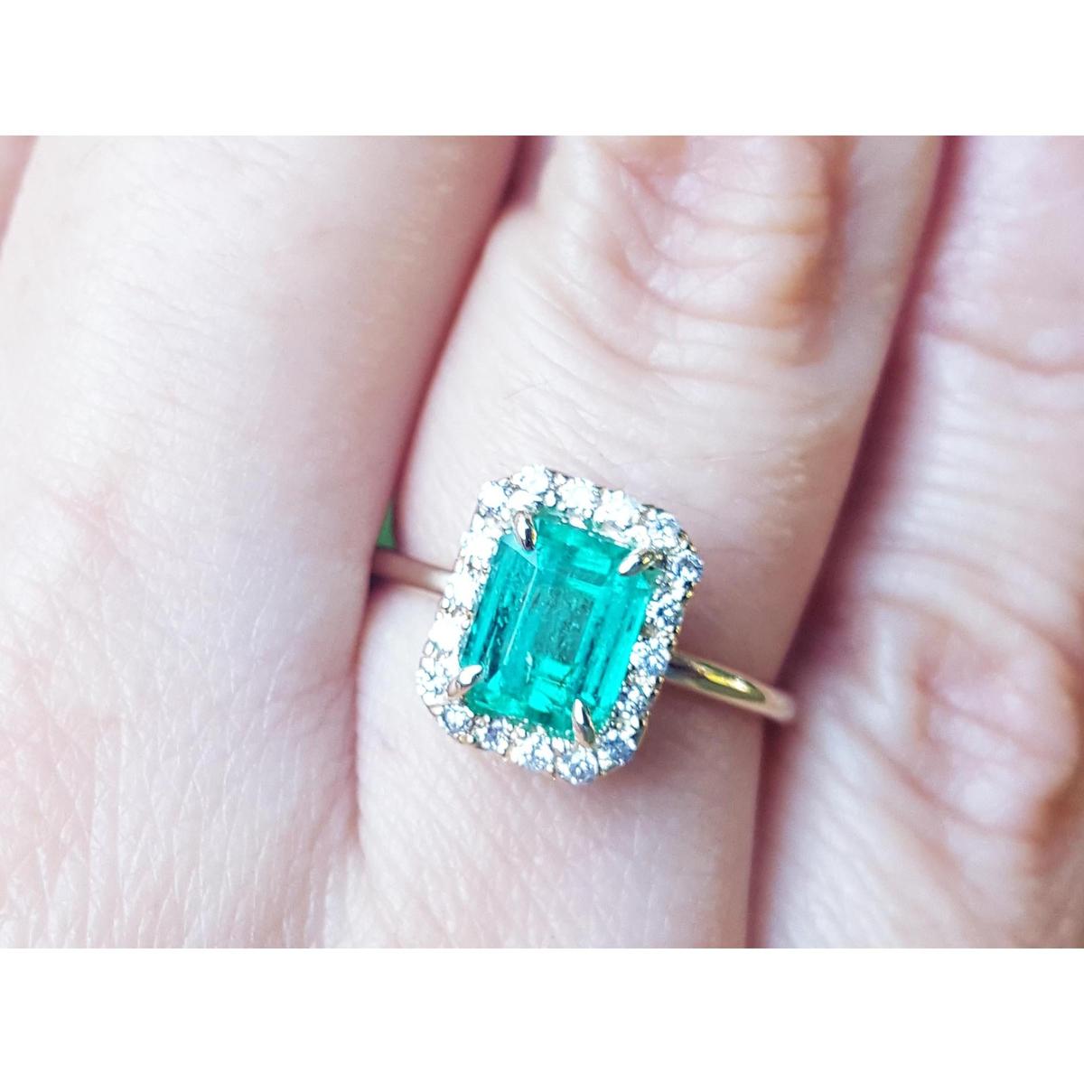 An emerald-cut halo diamond ring in yellow gold in a persons' finger.