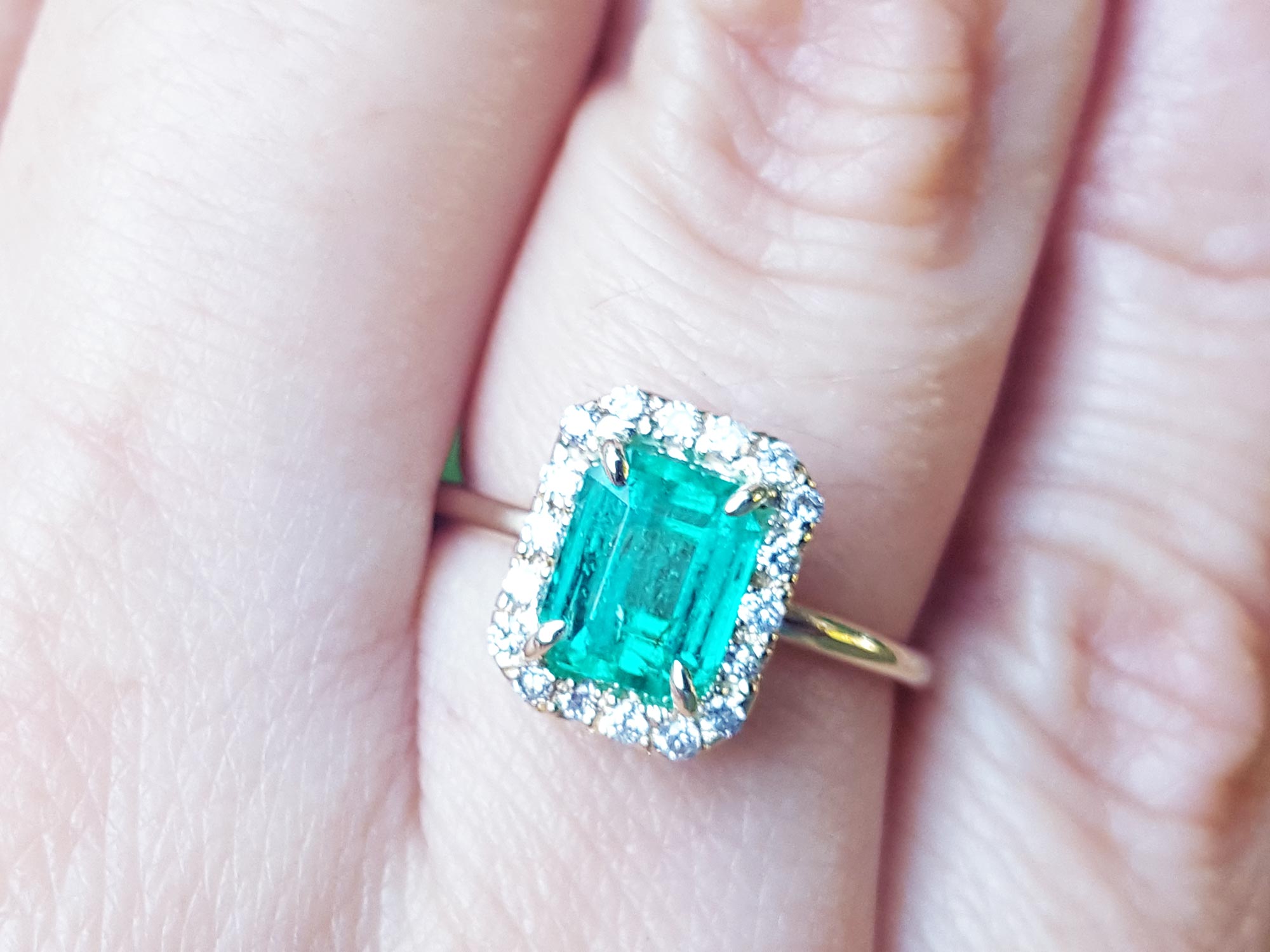 An emerald-cut halo diamond ring in yellow gold in a persons' finger.