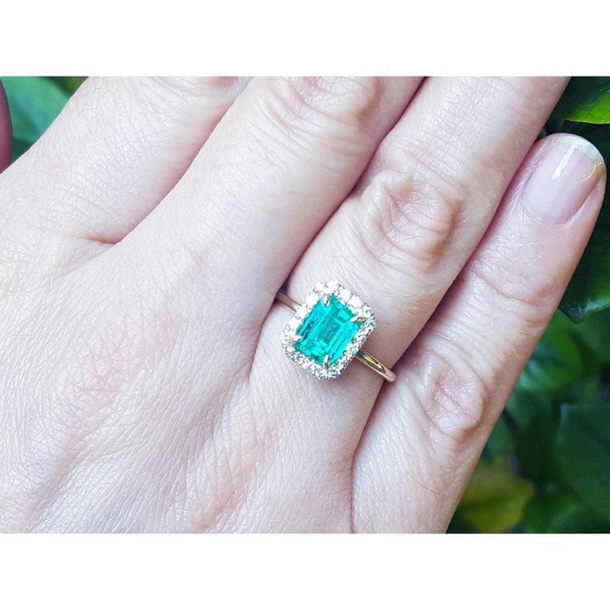 1.69 ct emerald-cut Colombian emerald ring with diamond halo in 14K yellow gold on a hand.