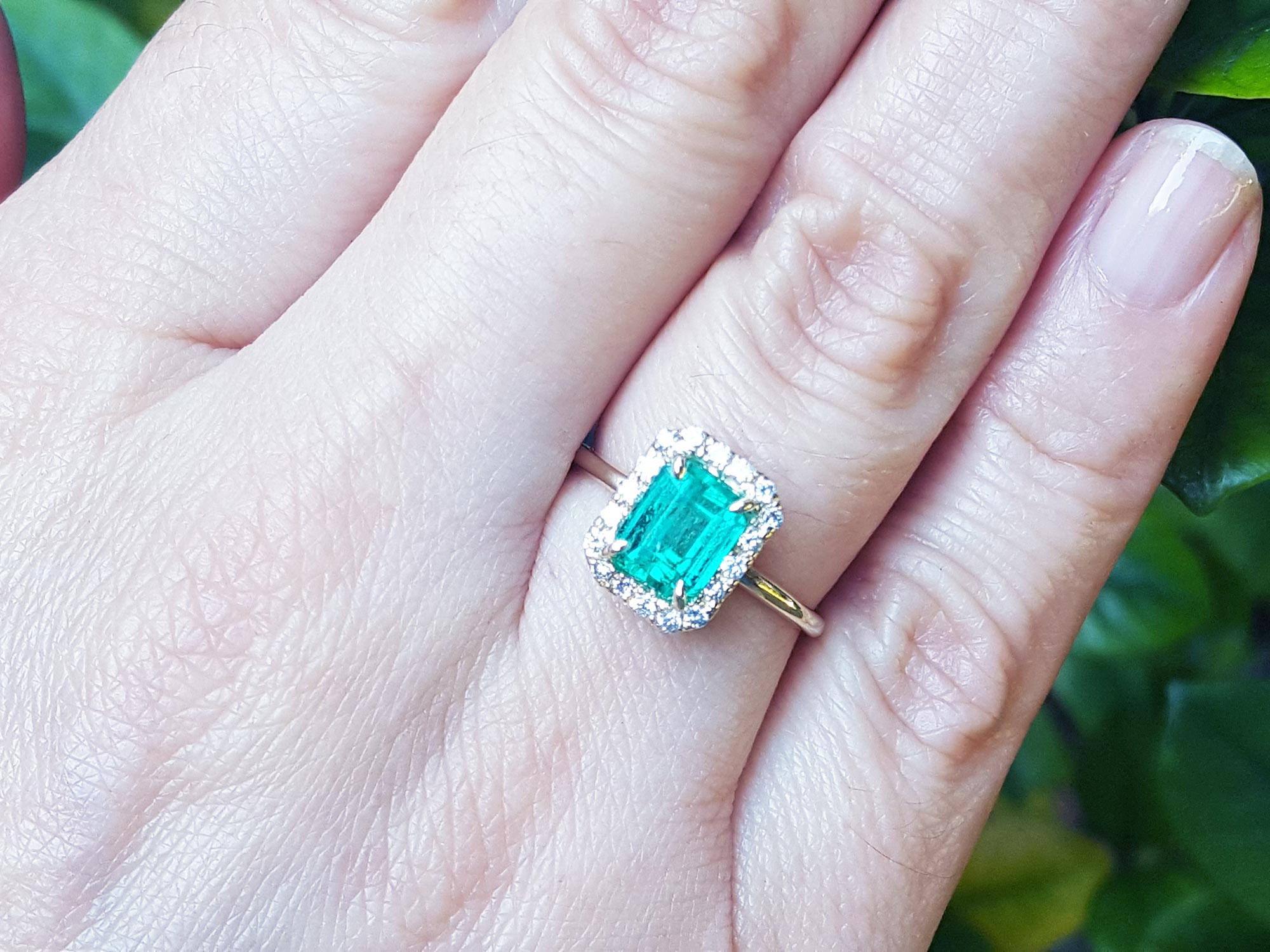 An emerald-cut emerald with a halo diamond ring on a person&#39;s hand.