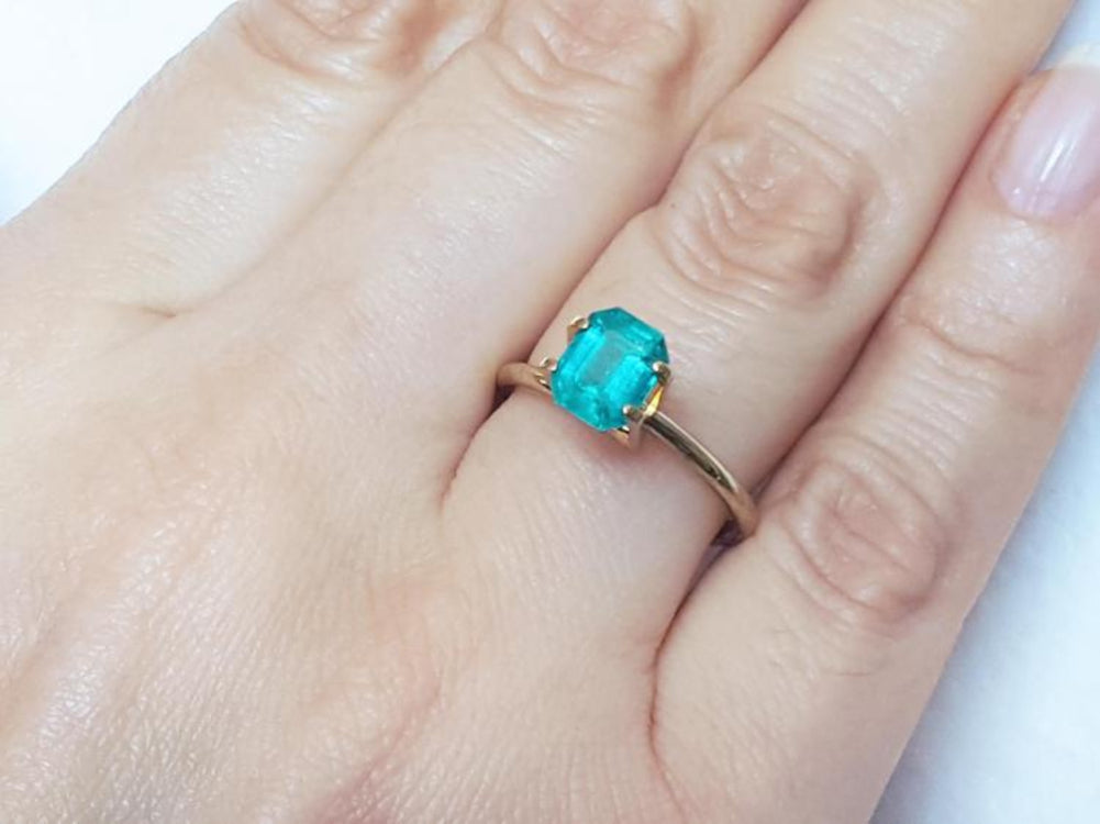 Emerald-cut Muzo Colombian emerald ring with a medium bluish-green gemstone set in a gold band on a hand.