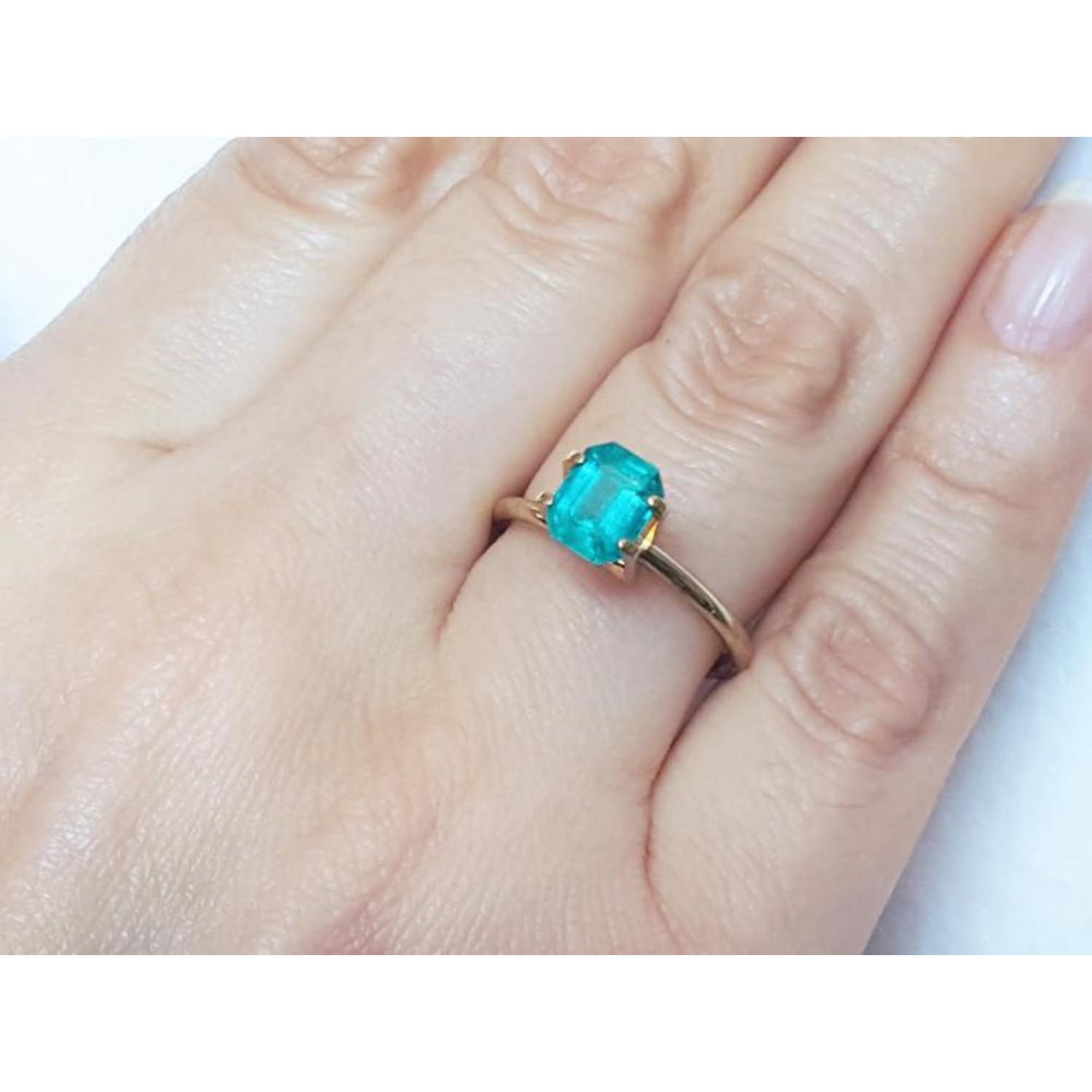Emerald-cut Muzo Colombian emerald ring with a medium bluish-green gemstone set in a gold band on a hand.