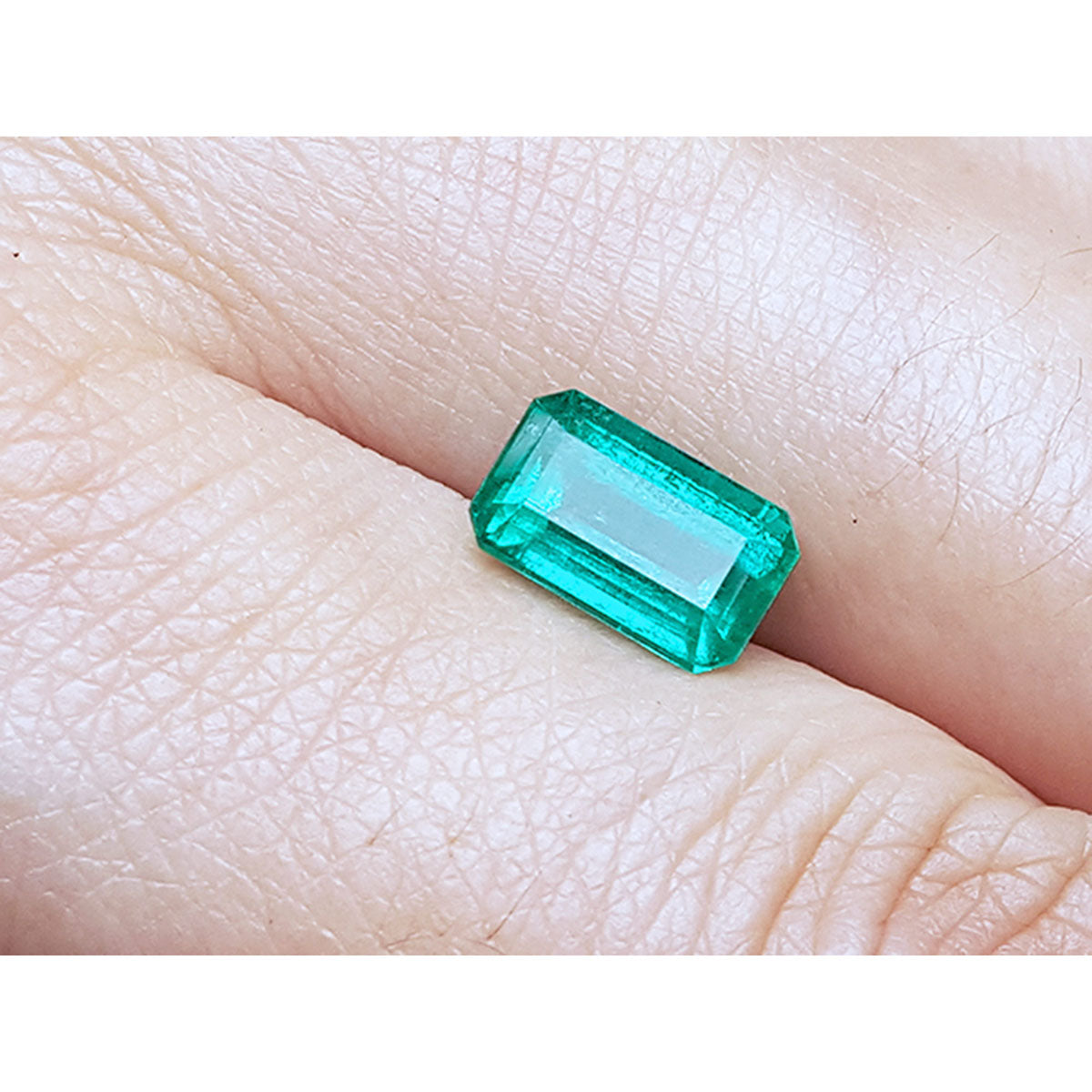 Emerald-cut natural loose colombian emerald, front position table and crown visibles between two fingers