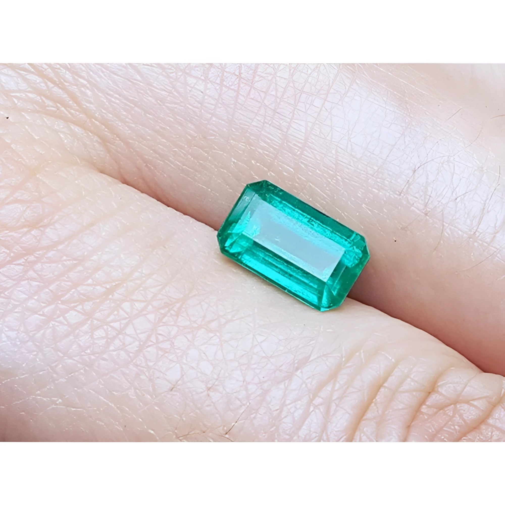 2.55-carat emerald-cut natural Colombian emerald with a medium deep green hue, held in a hand.