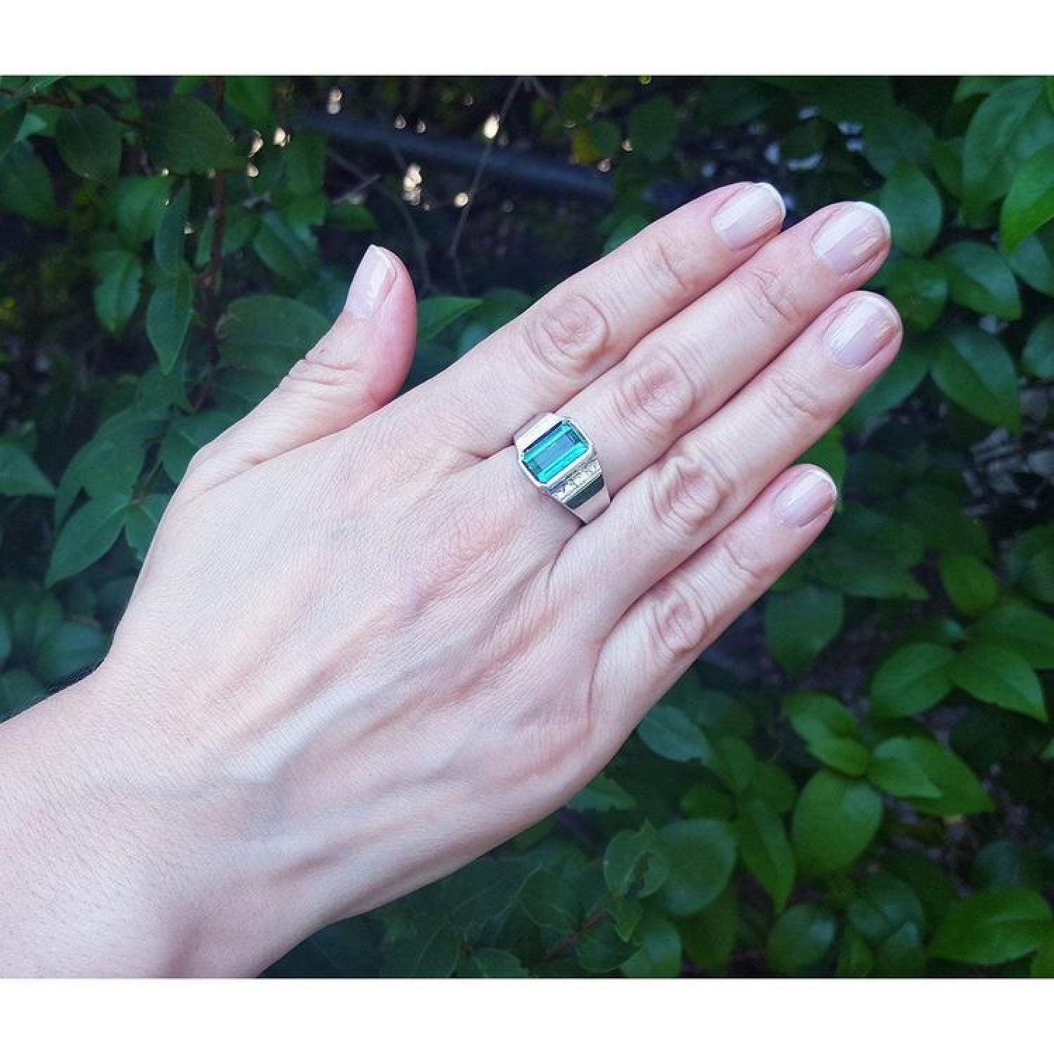 Emerald-cut men's emerald ring with side diamonds, bezel set in 18K white gold on a hand.