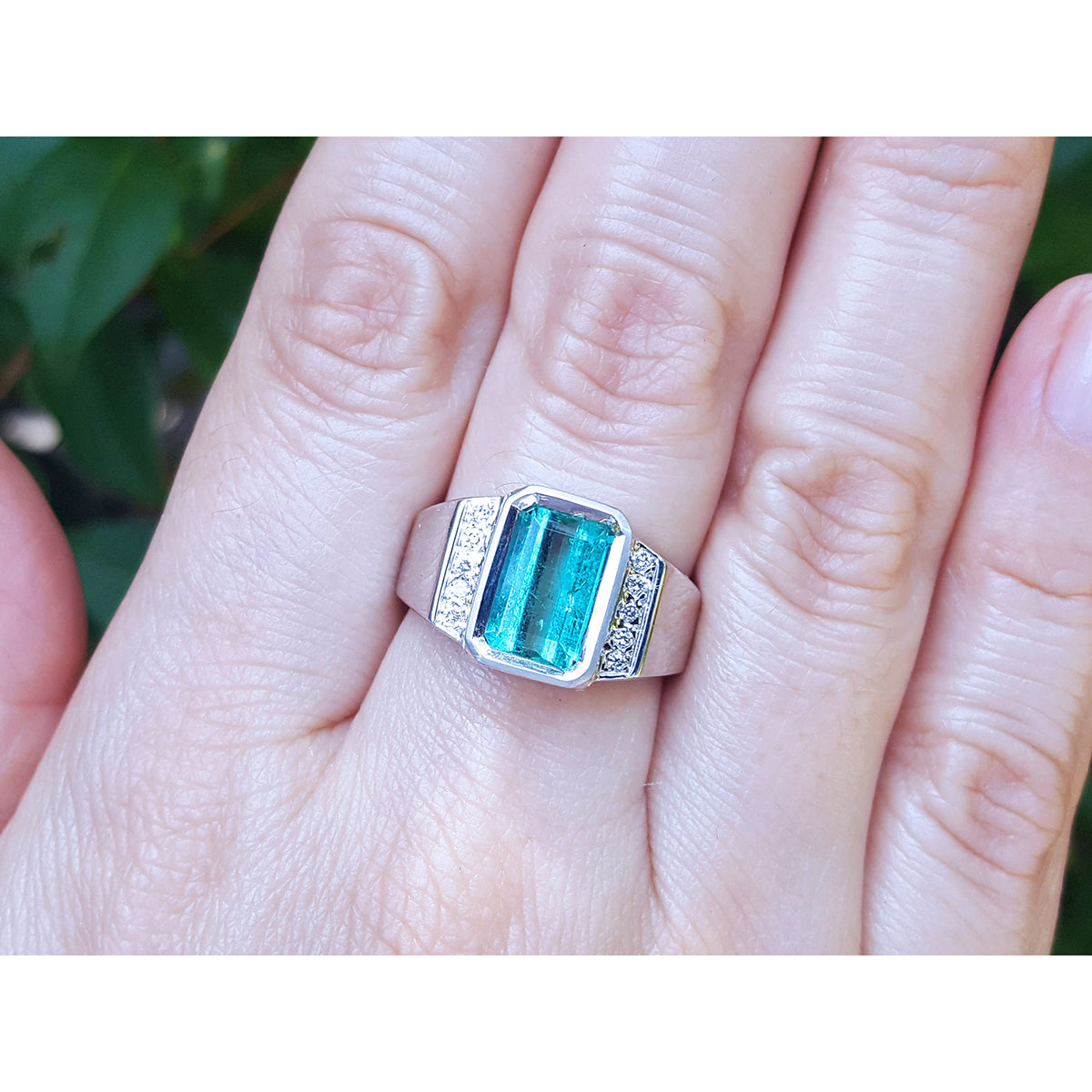 A men&#39;s emerald ring in white gold on a person&#39;s finger against a natural background.