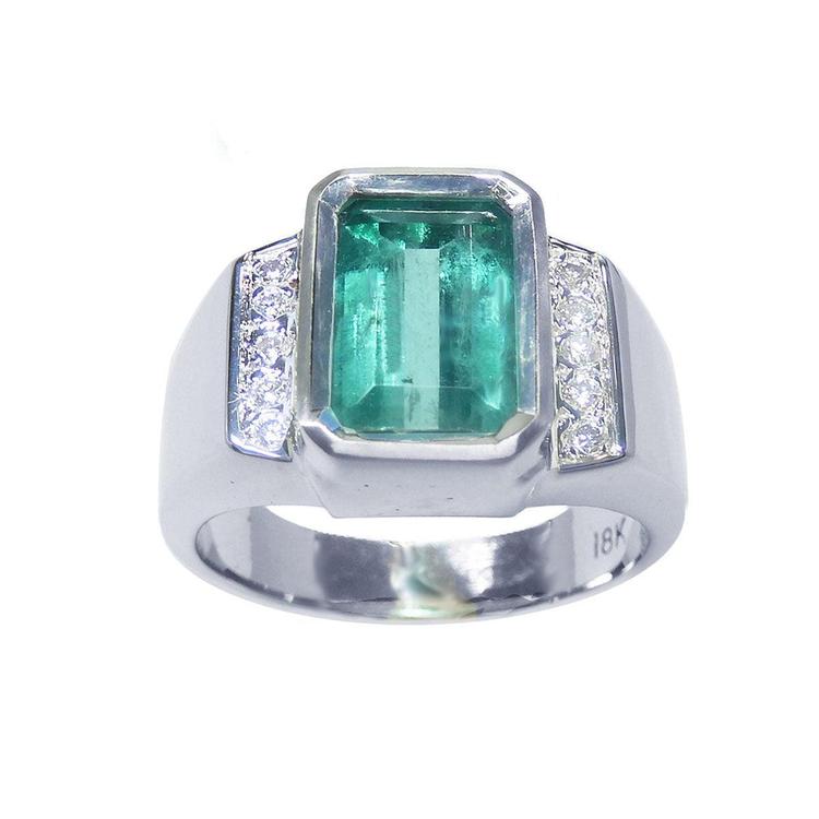 A 18k white gold mens ring with an emerald cut natural colombian emerald bezel set and diamond accents on a topside view and sideways visibles.