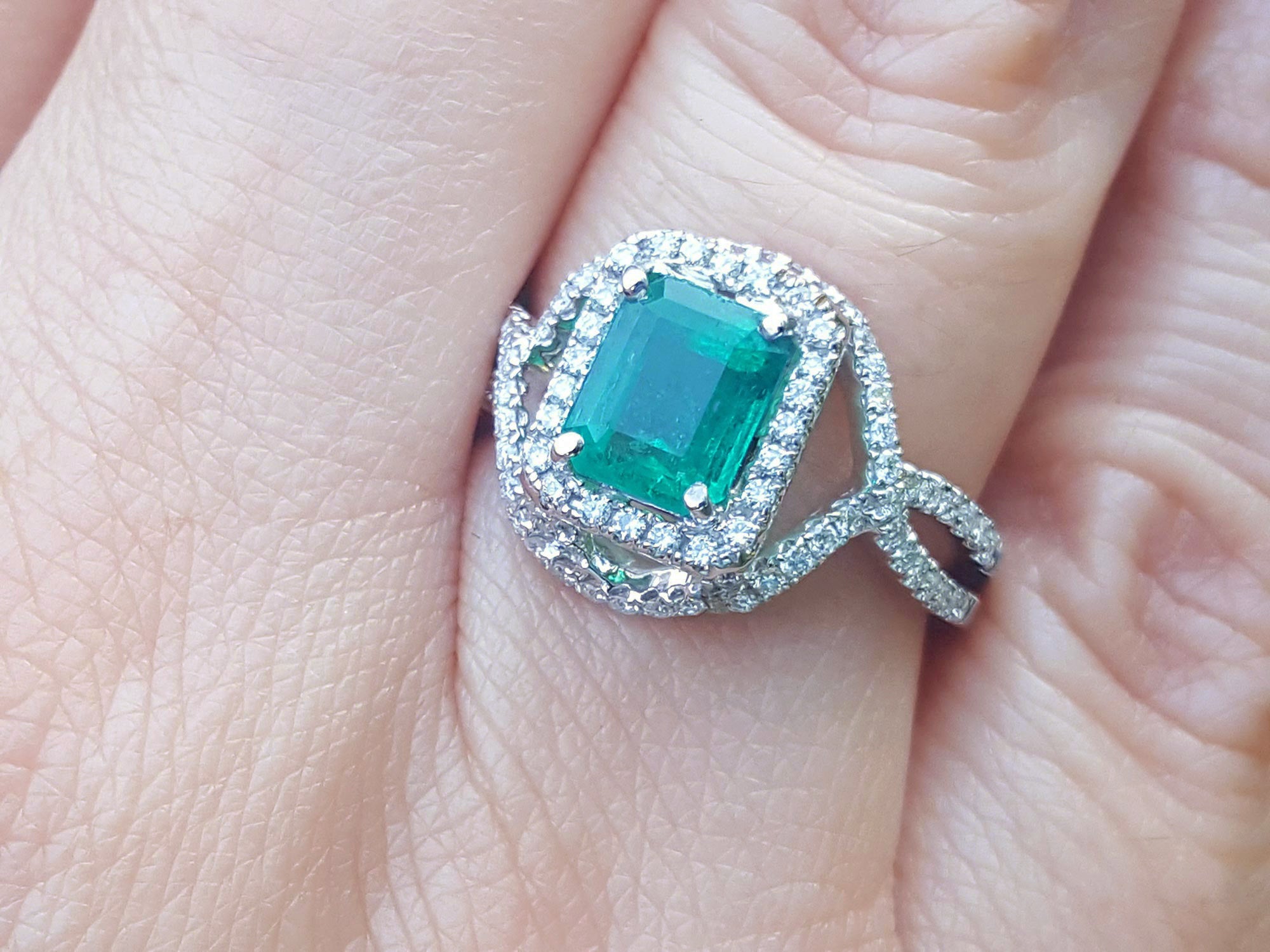 
A square emerald ring with diamond accents on a finger.