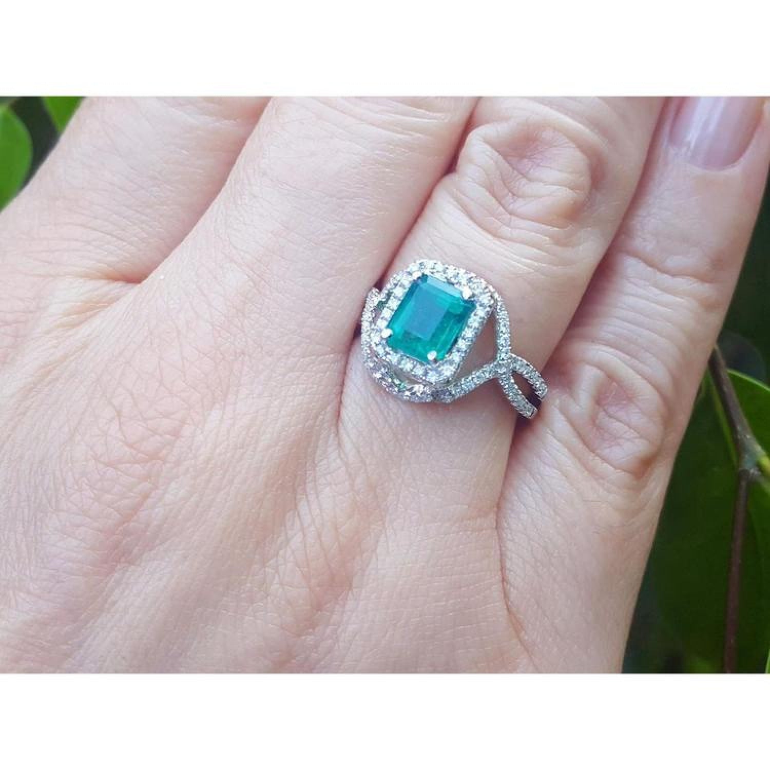 Emerald-cut natural emerald ring with halo diamonds on an 18K white gold split shank band.