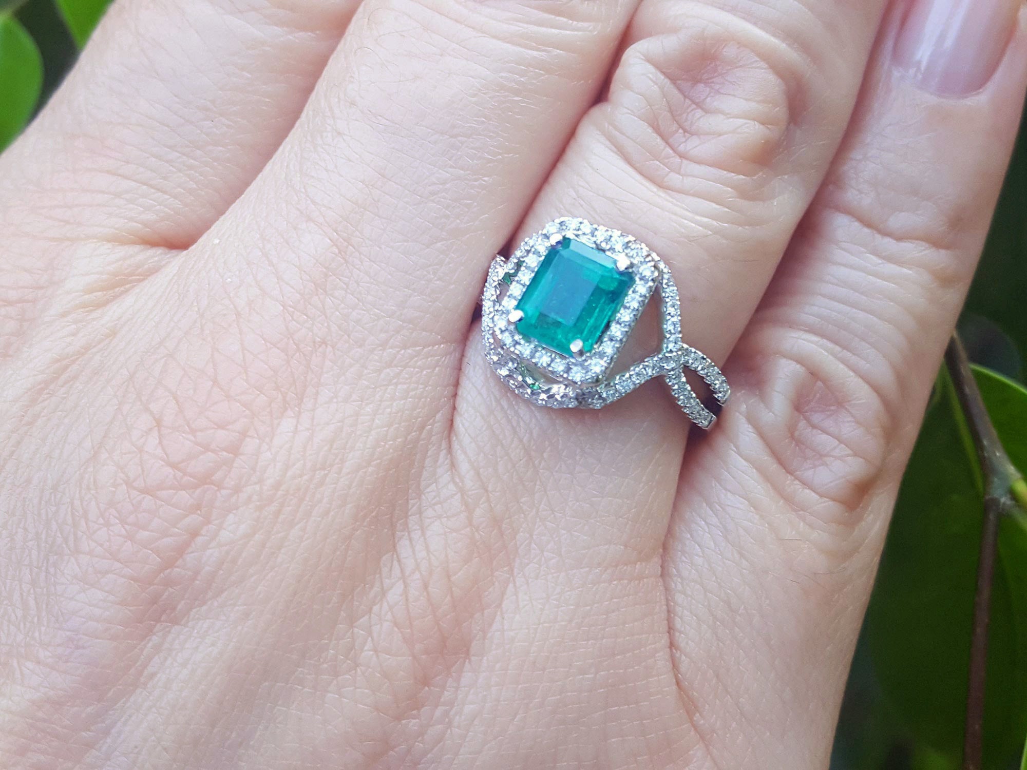 Ring with a real colombian emerald and accent diamonds on a hand against a natural background.