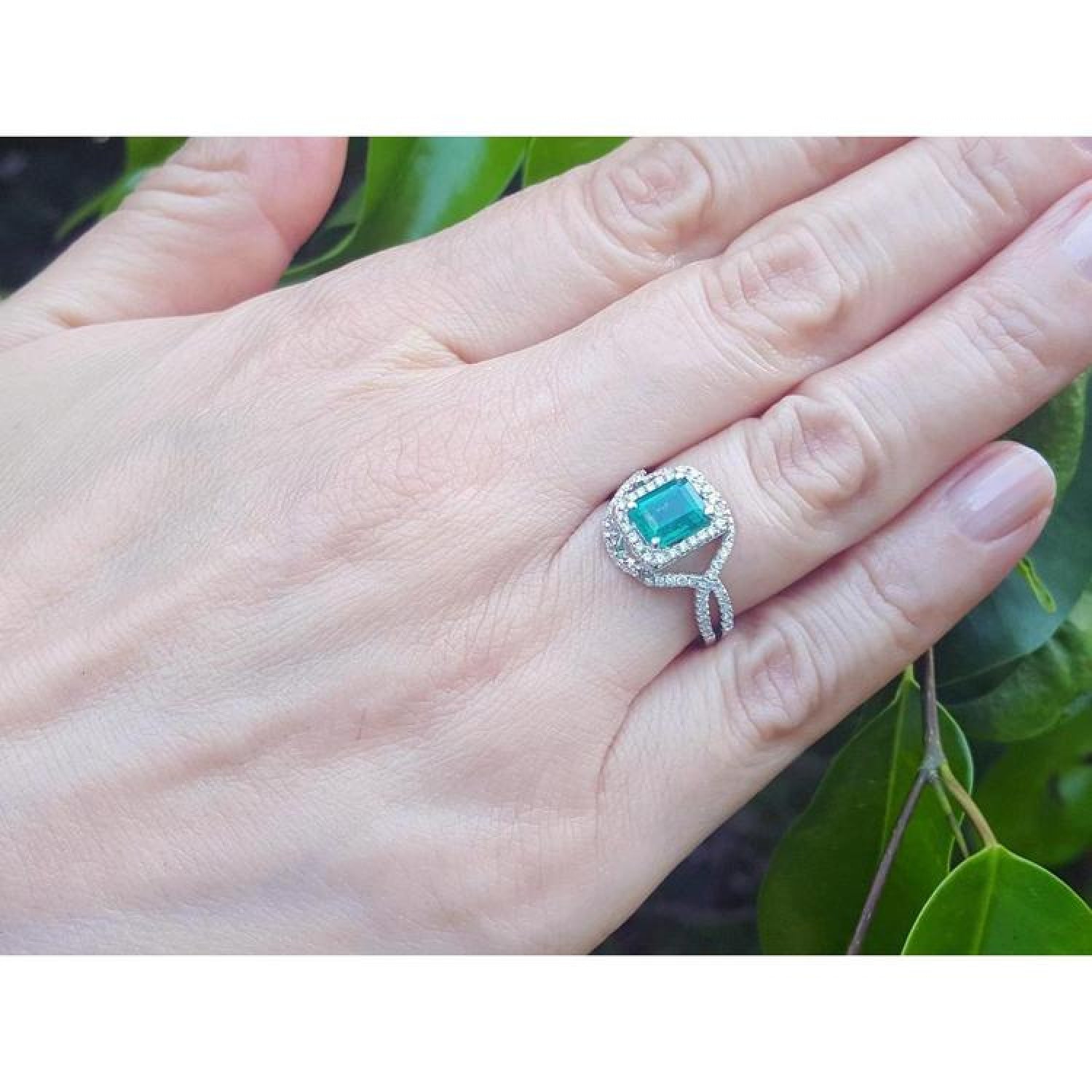 Emerald-cut natural emerald ring with halo diamonds on an 18K white gold split shank band.