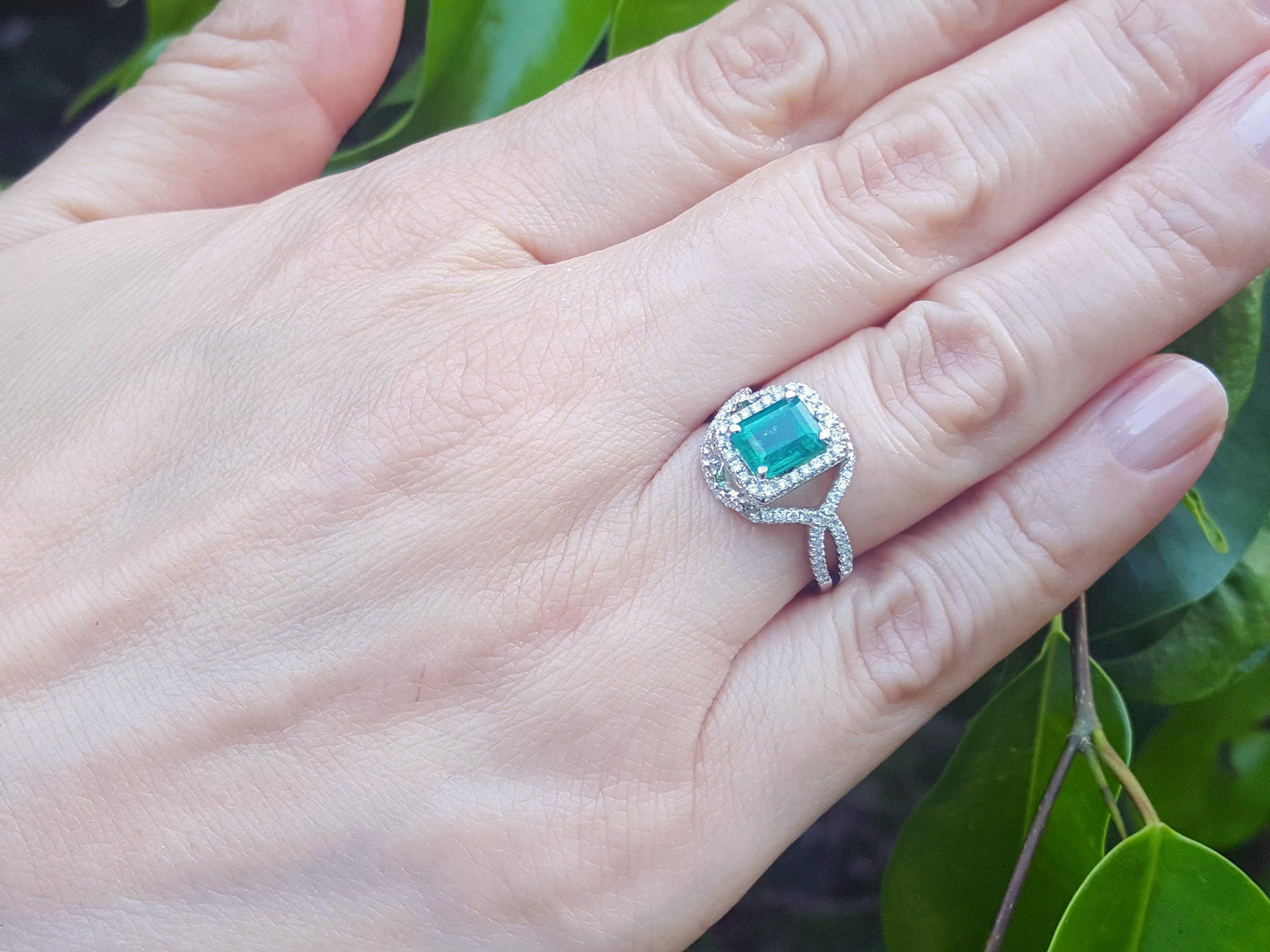 Hand wearing a brides&#39; May birthstone emerald ring against a leafy background.