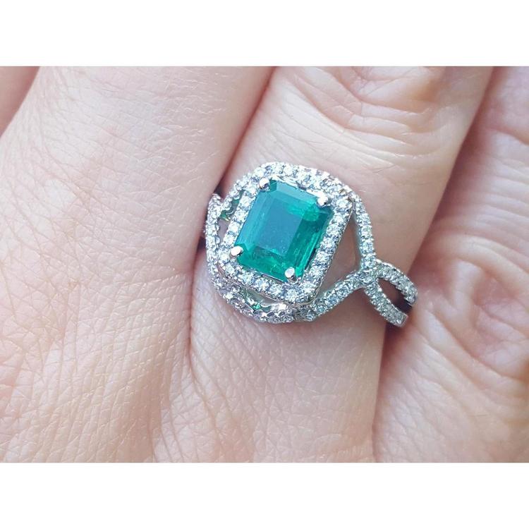 
A square emerald ring with halo diamond accents in 18k white gold on a finger.