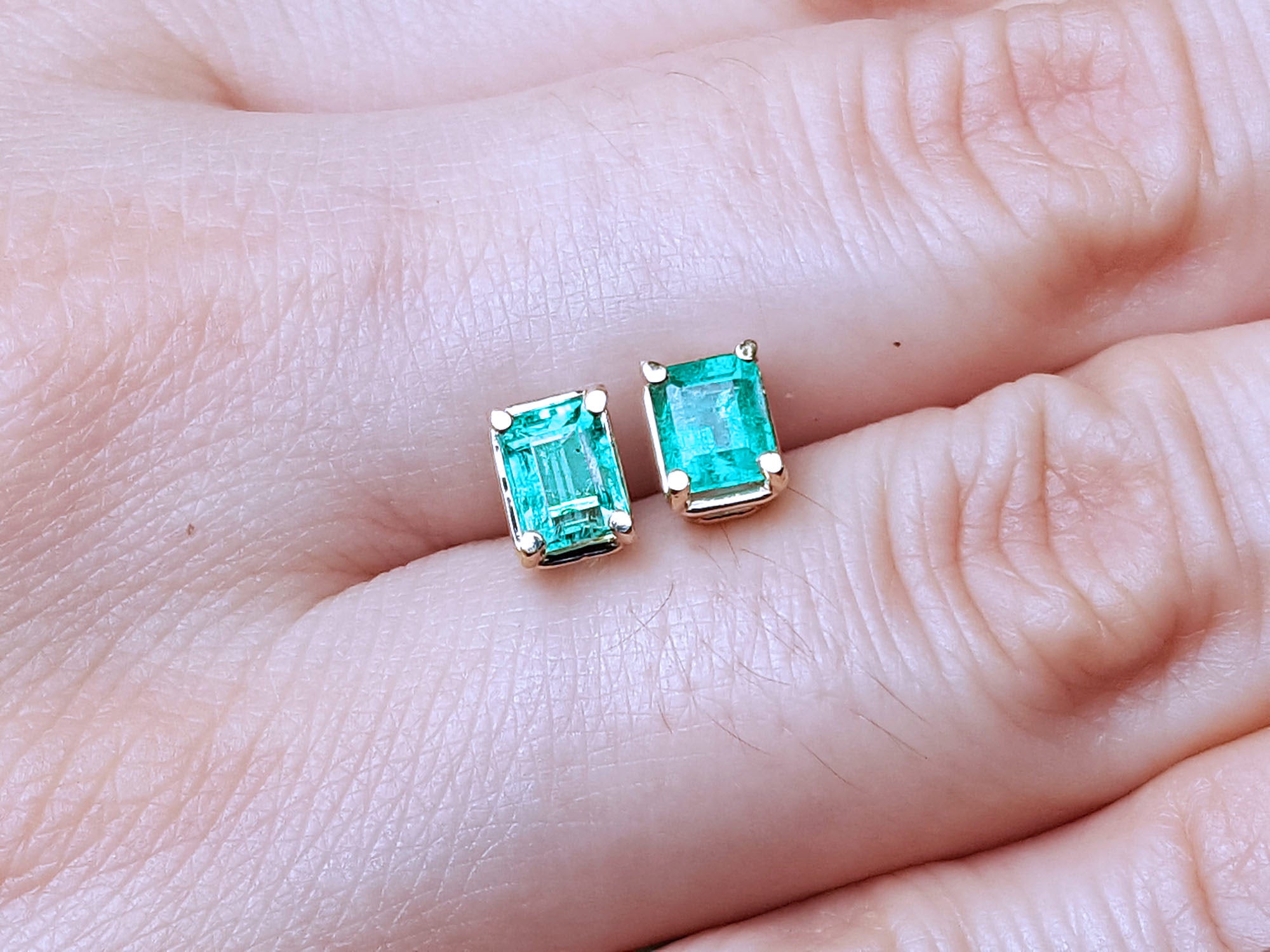Emerald-cut emerald stud earrings between fingers.