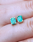 Emerald-cut emerald stud earrings between fingers.