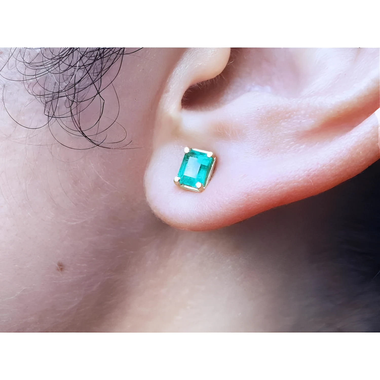 Emerald-cut natural emerald stud earring in 14K yellow gold, worn on an ear.