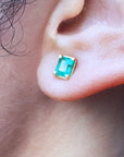 Close-up of a woman's ear wearing aemerald-cut stud emerald earring with yellow gold frame.