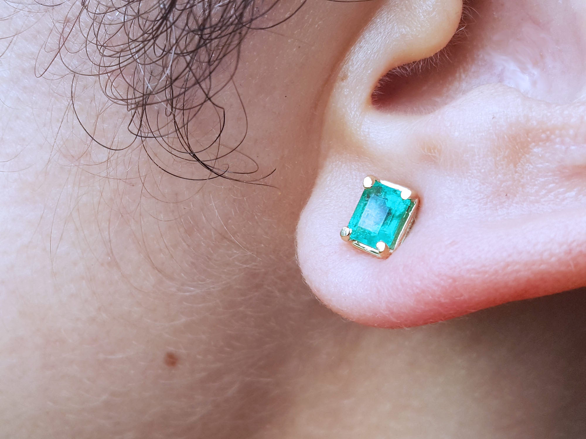 Close-up of an earlobe wearing a emerald stud earring.