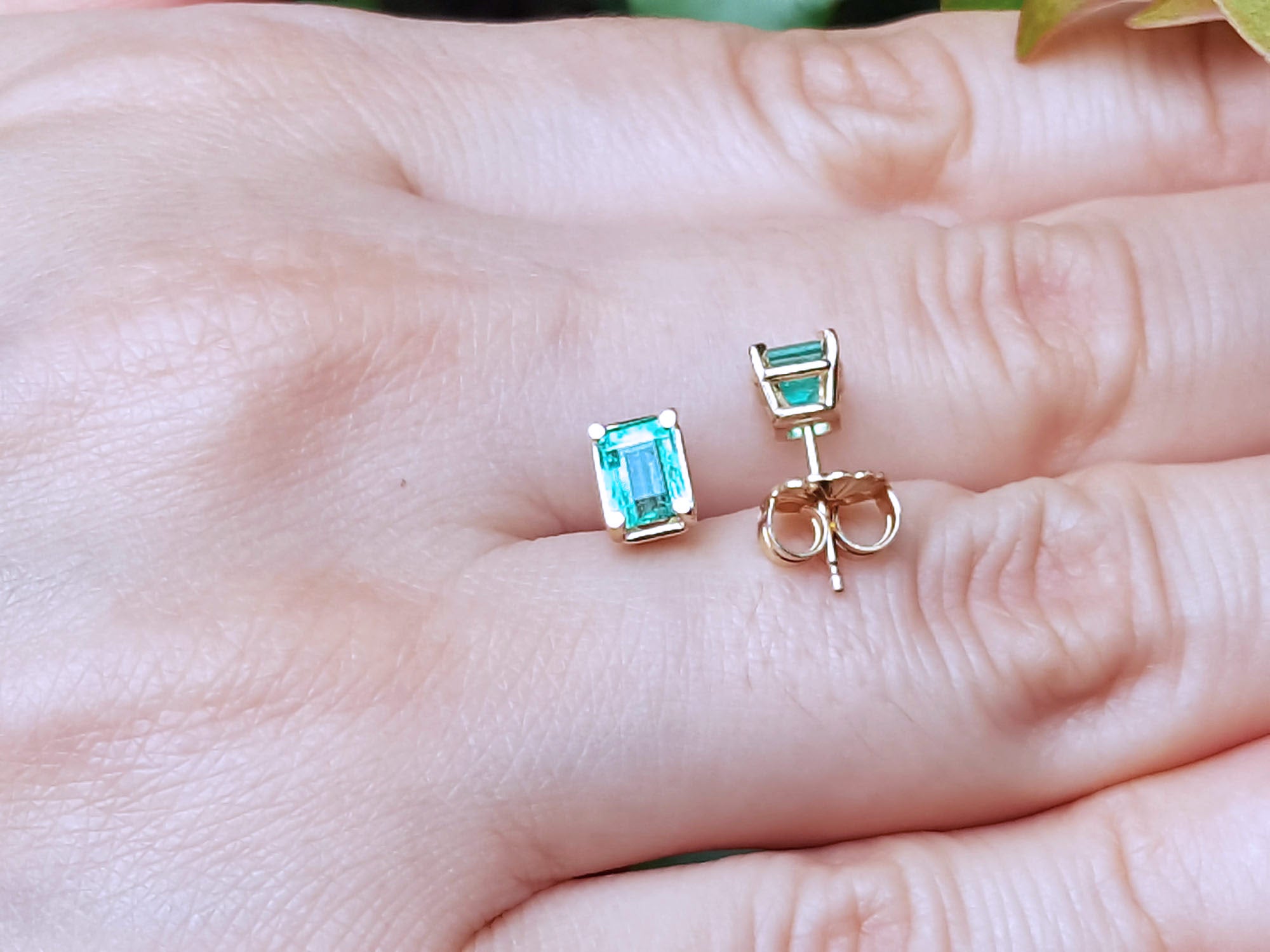 Push backs emerald stud earrings on a hand.