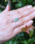 Hand displaying a pair of emerald-cut emerald stud earrings with a natural background of leaves.