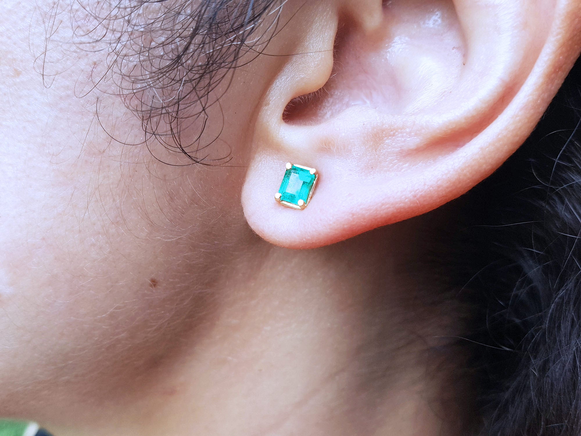 Close-up of an ear wearing a emerald-cut stud emerald earring with yellow gold frame.