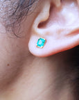 Close-up of an ear wearing a emerald-cut stud emerald earring with yellow gold frame.