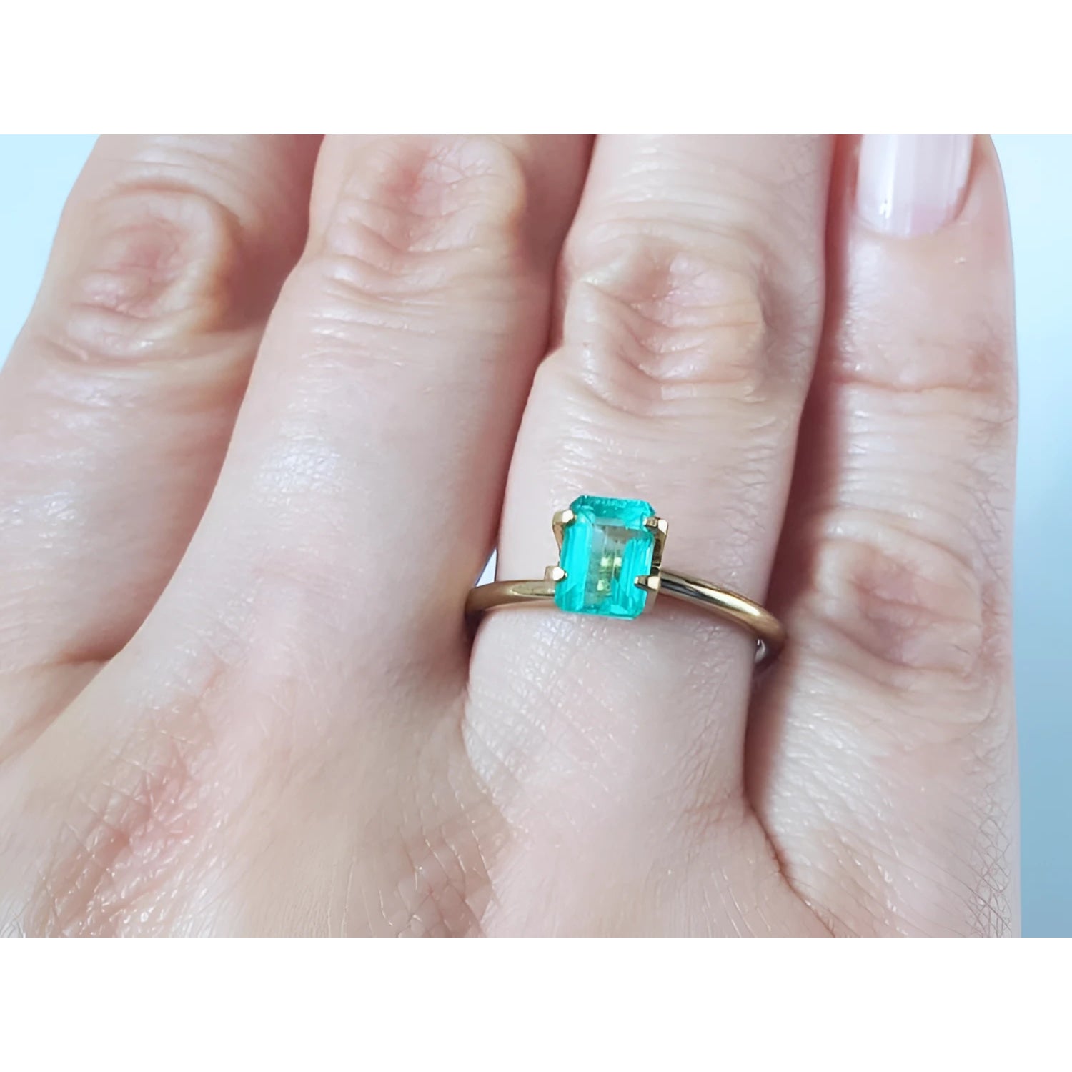 1.13 carat emerald-cut Muzo Colombian emerald set in a simple gold ring on a hand.