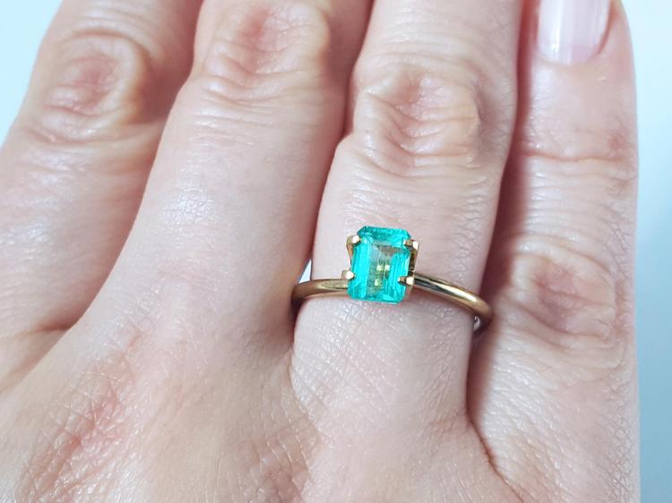 1.13 carat emerald-cut Muzo Colombian emerald set in a simple gold ring on a hand.