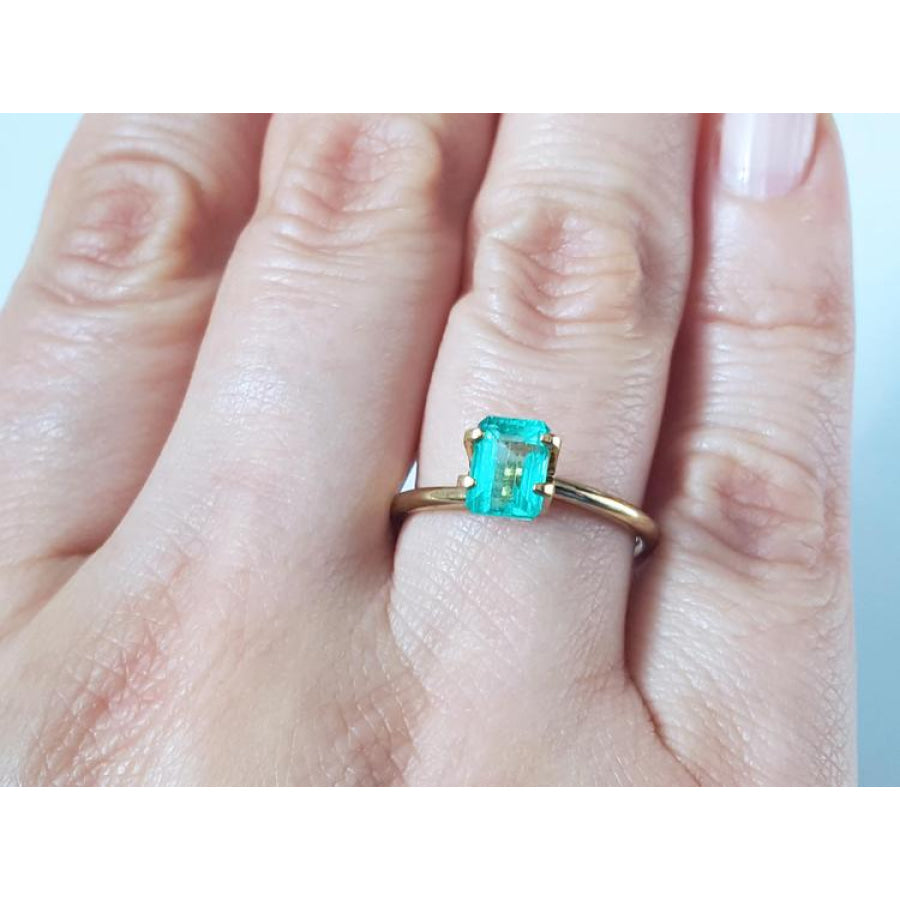 1.13 carat emerald-cut Muzo Colombian emerald set in a simple gold ring on a hand.