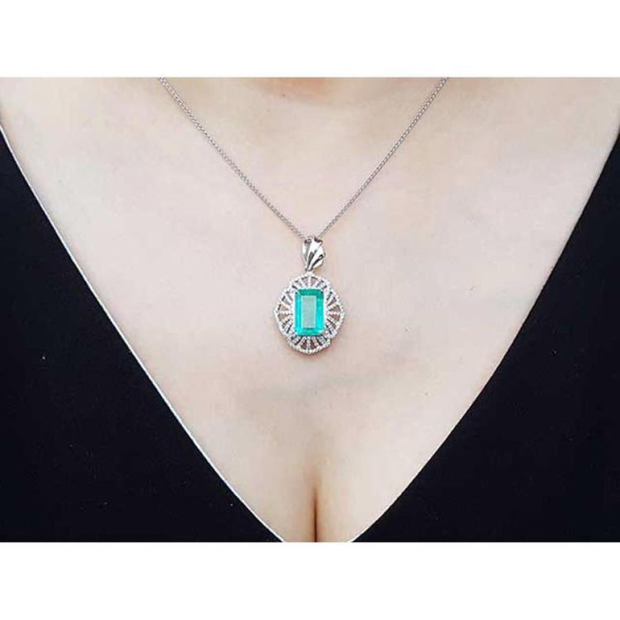 Emerald-cut emerald pendant with natural diamonds on a 14K white gold chain, worn on a woman's neck.