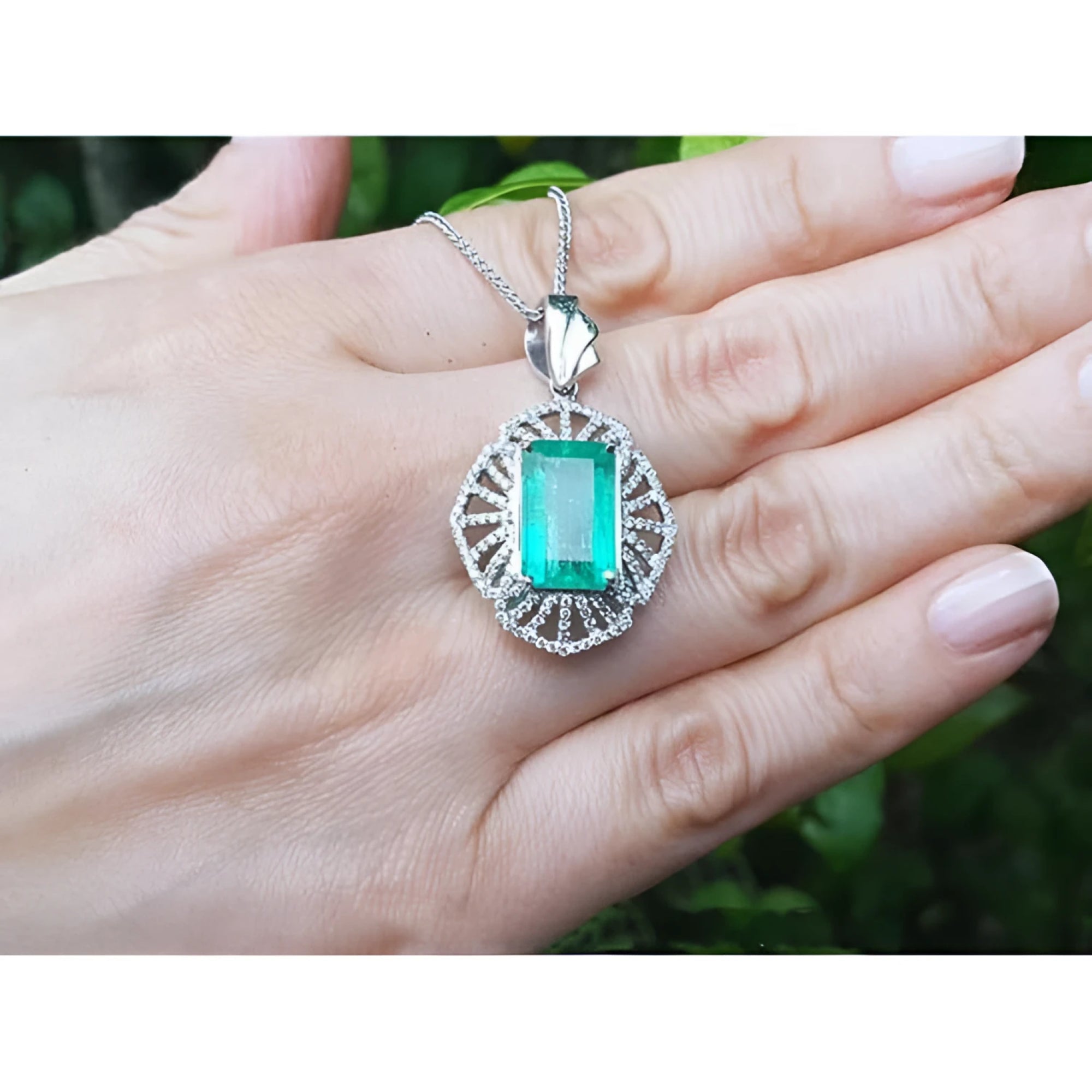 Emerald-cut Colombian emerald pendant with natural diamonds in 14K white gold, held on a hand.