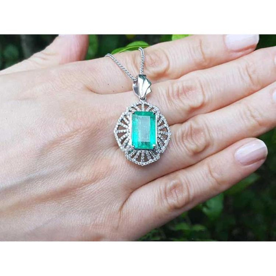 Emerald-cut Colombian emerald pendant with natural diamonds in 14K white gold, held on a hand.