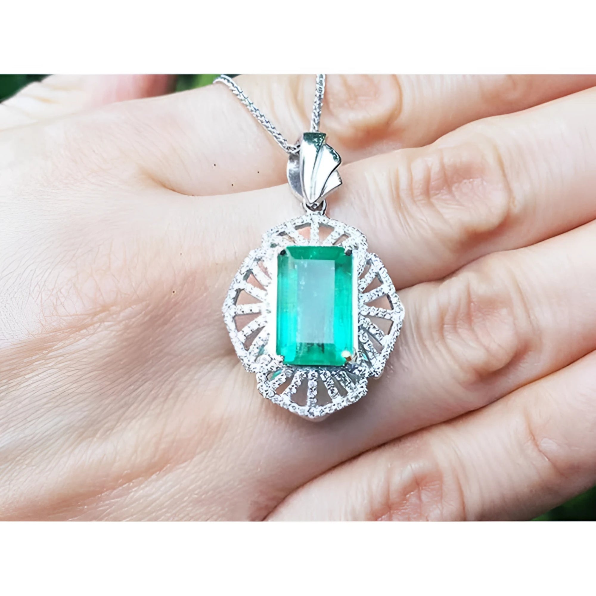 Emerald-cut emerald pendant with natural diamonds in 14K white gold, held by a hand.