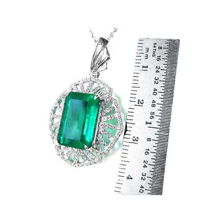 Emerald green gemstone pendant with white gold chain, next to a ruler for scale.