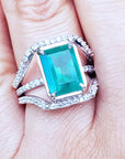 Women's emerald ring white gold with three rows of diamonds on a finger.