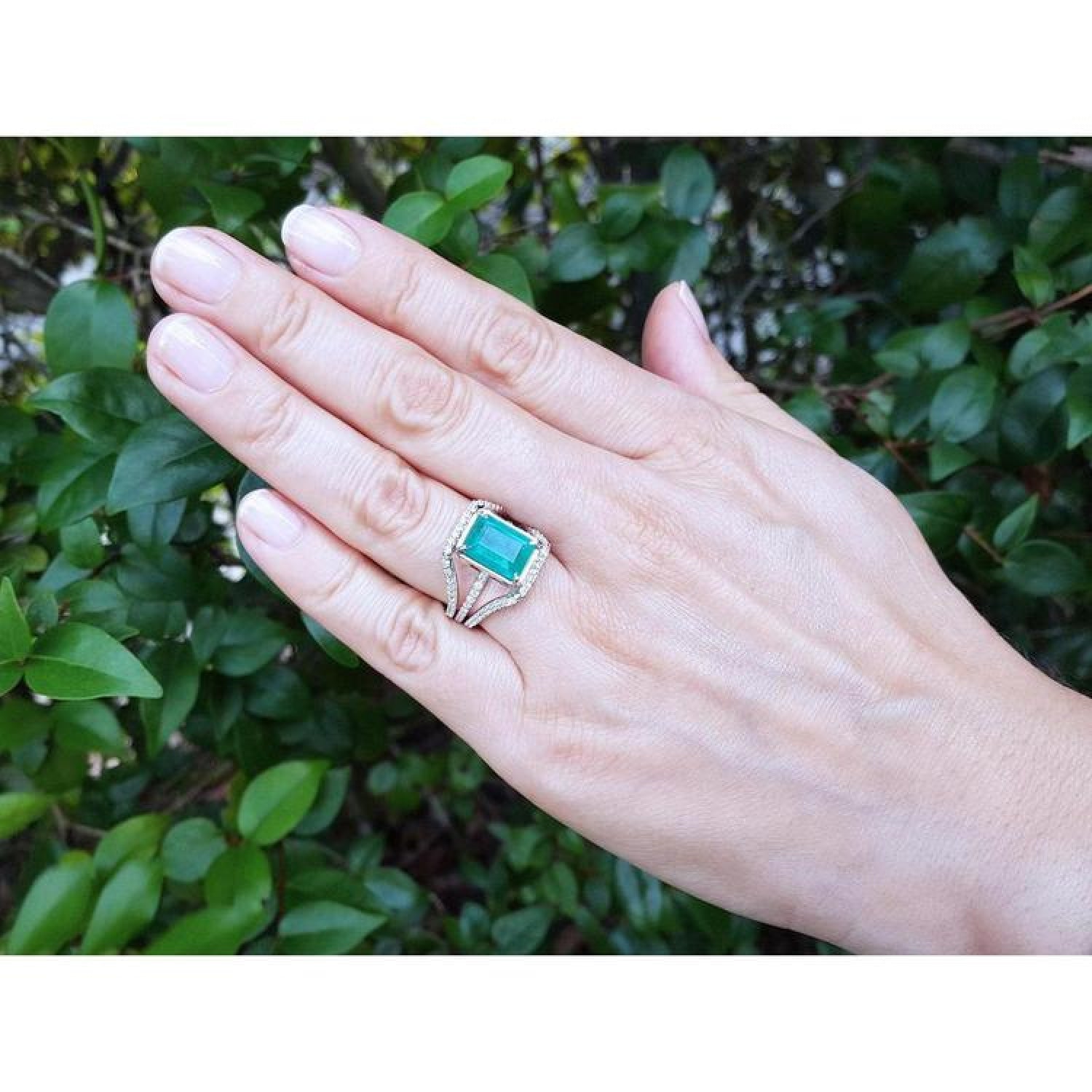Emerald-cut 3.90 ct bluish-green emerald ring with triple diamond rows in 14K white gold on a hand.