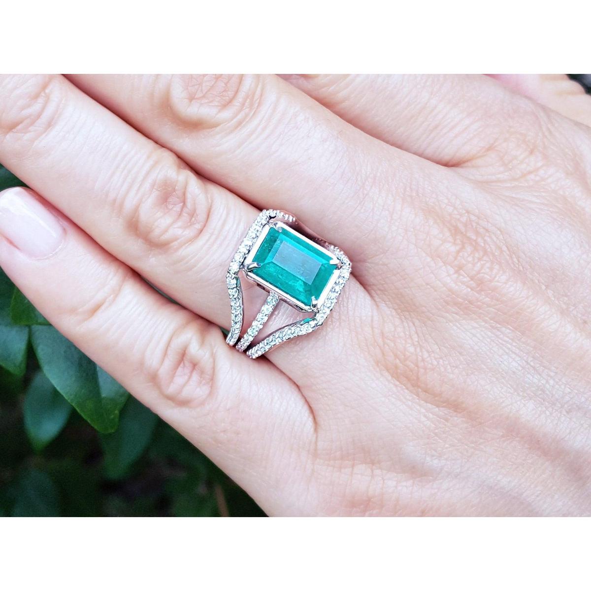Ring with an emerald-cut emerald ring on a hand against a blurred natural background.