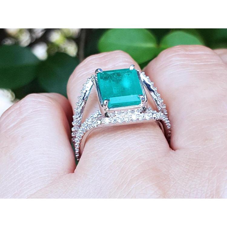Emerald-cut 3.90 ct bluish-green emerald ring with triple diamond rows in 14K white gold on a finger.