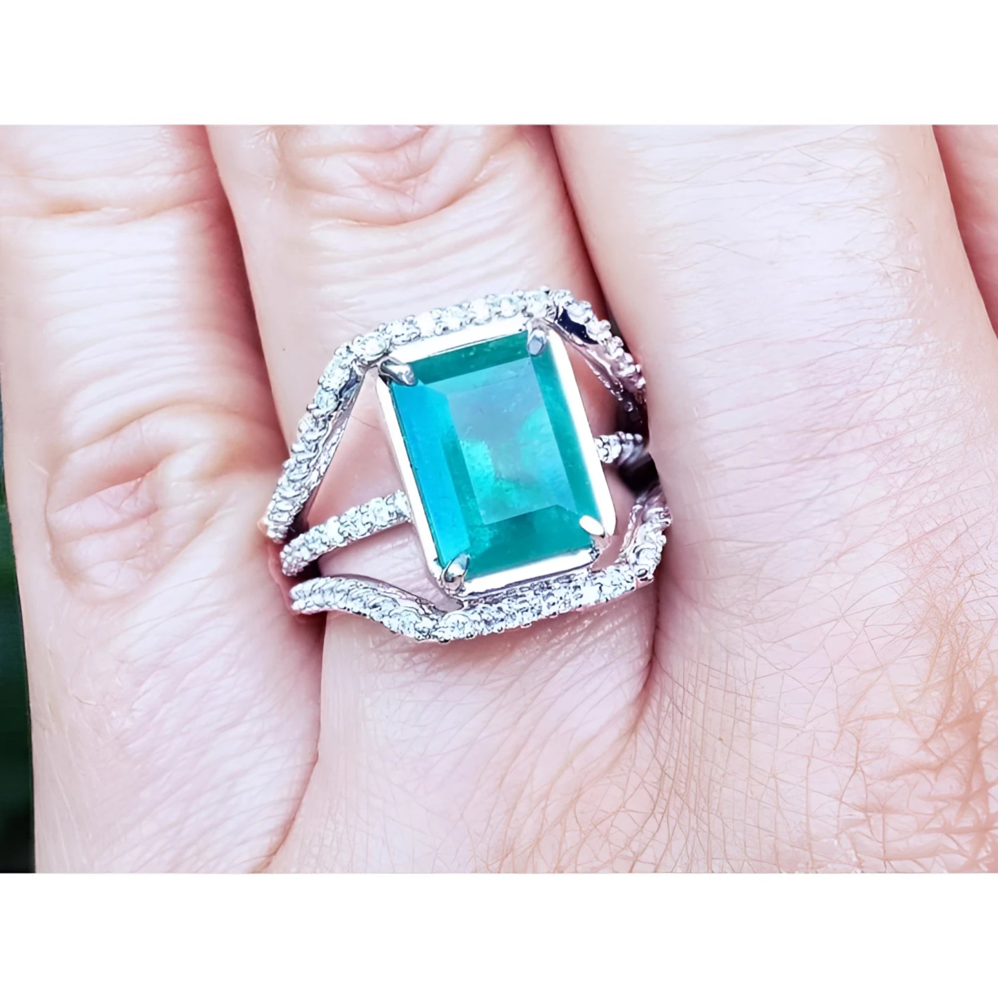 Women's emerald ring in 14k white gold with three rows of natural diamonds on a finger.